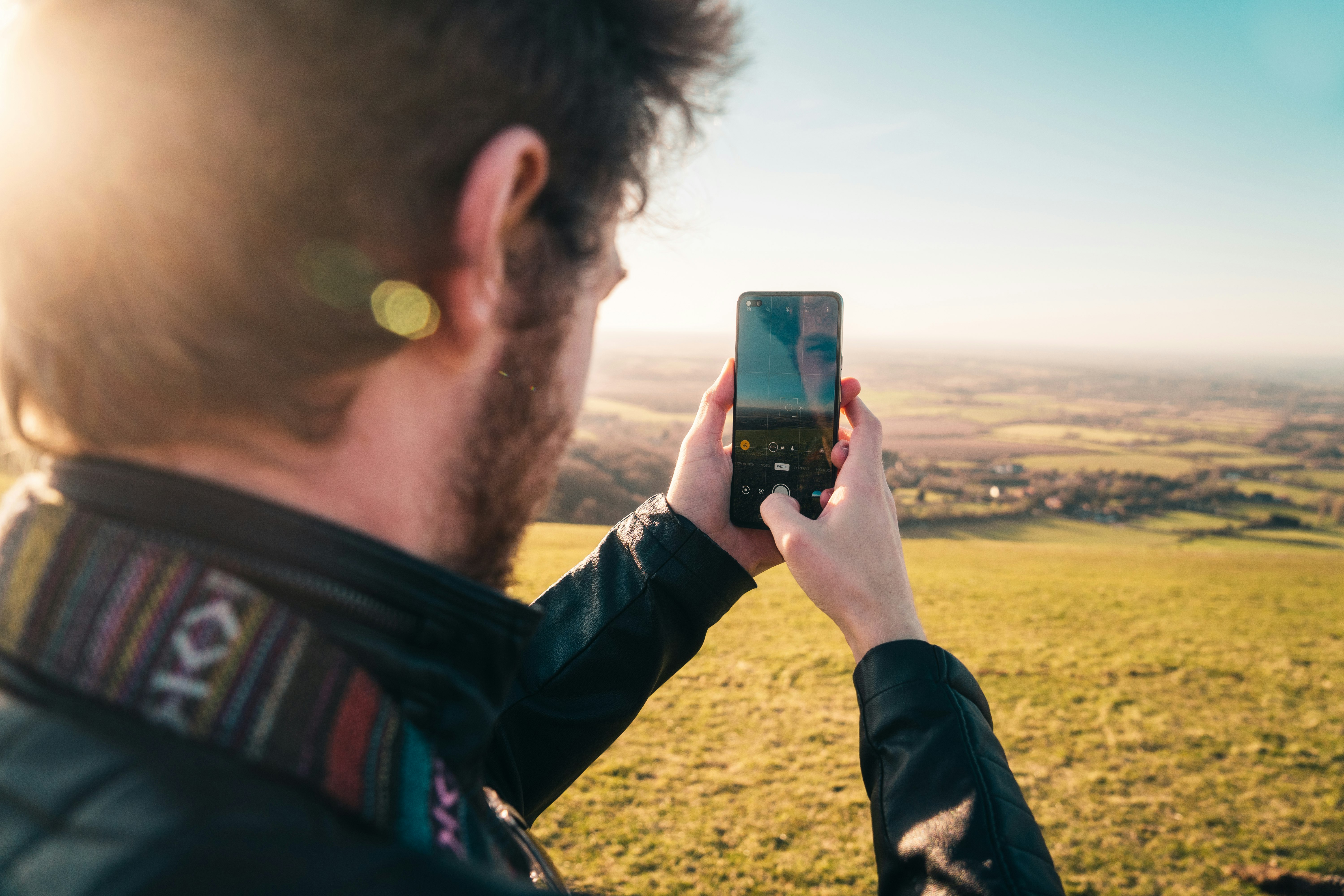 man in black jacket taking photo of green grass field during daytime